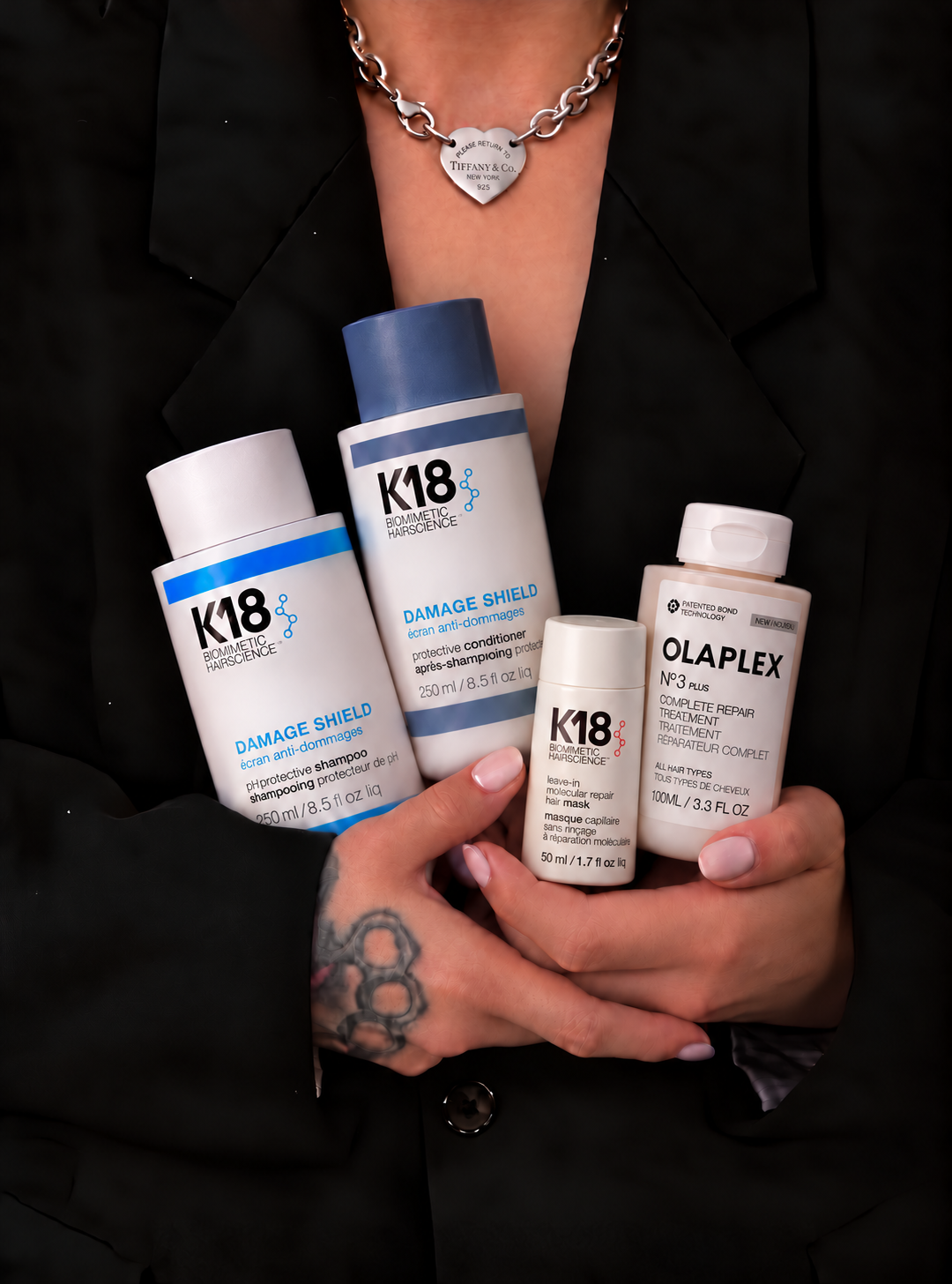 Cris holding the Fall Repair Routine products: K18 Leave-In Mask, Olaplex Nº.3PLUS, K18 Damage Shield shampoo and conditioner
