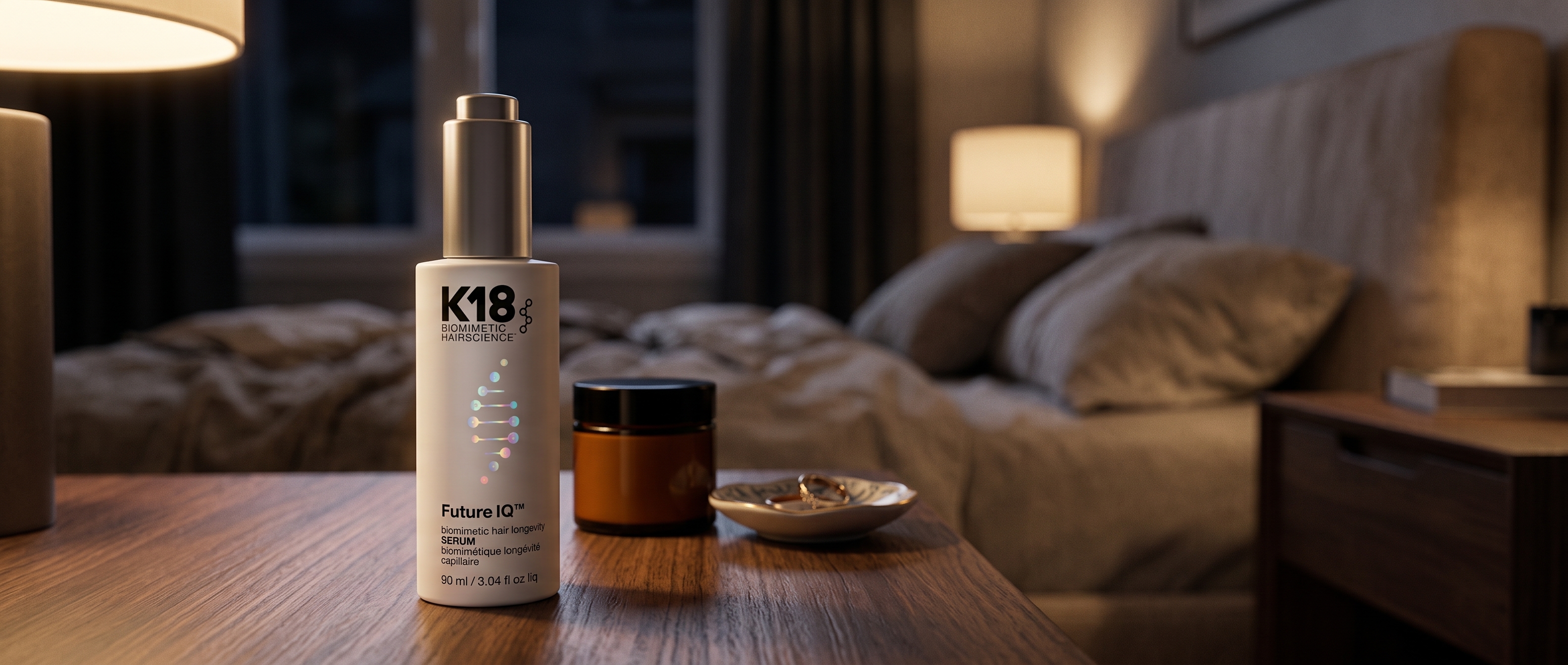 K18 FutureIQ serum bottle on a nightstand at night, beside skincare, with warm light and an elegant bedroom in the background